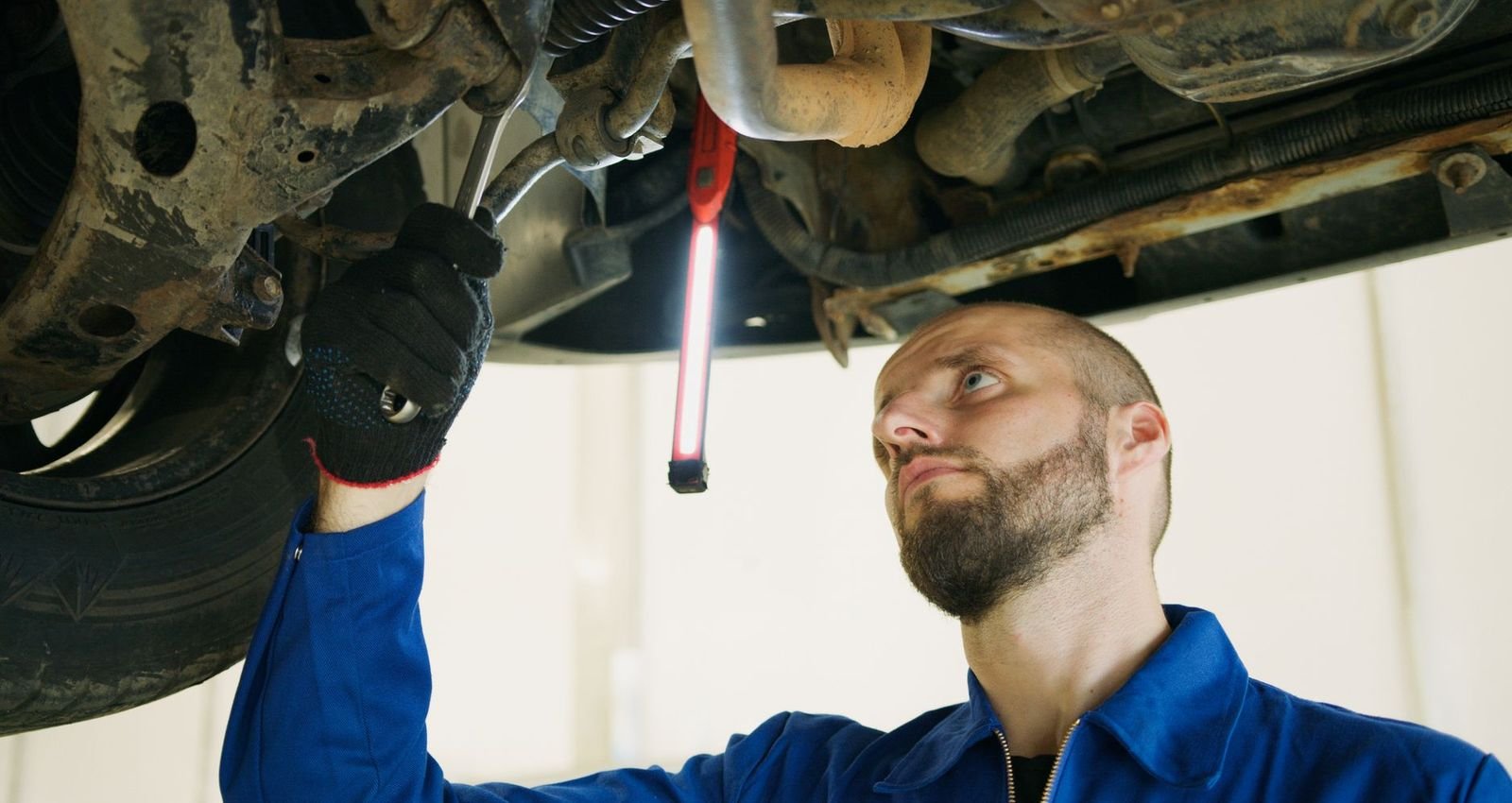 A mechanic under a car inspecting it with a flashlight