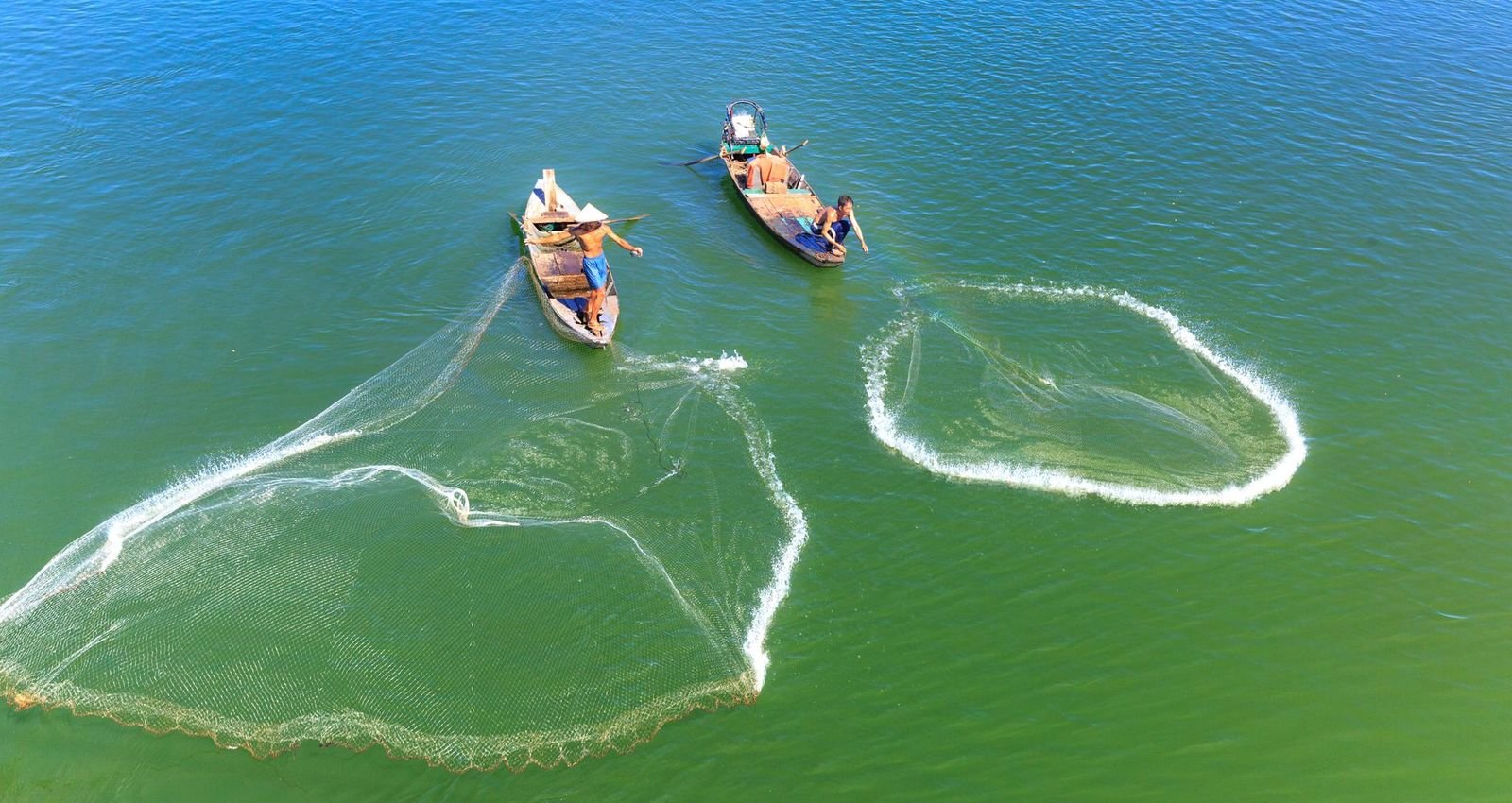 Aerial view of two fishing boats casting wide nets on bright green water
