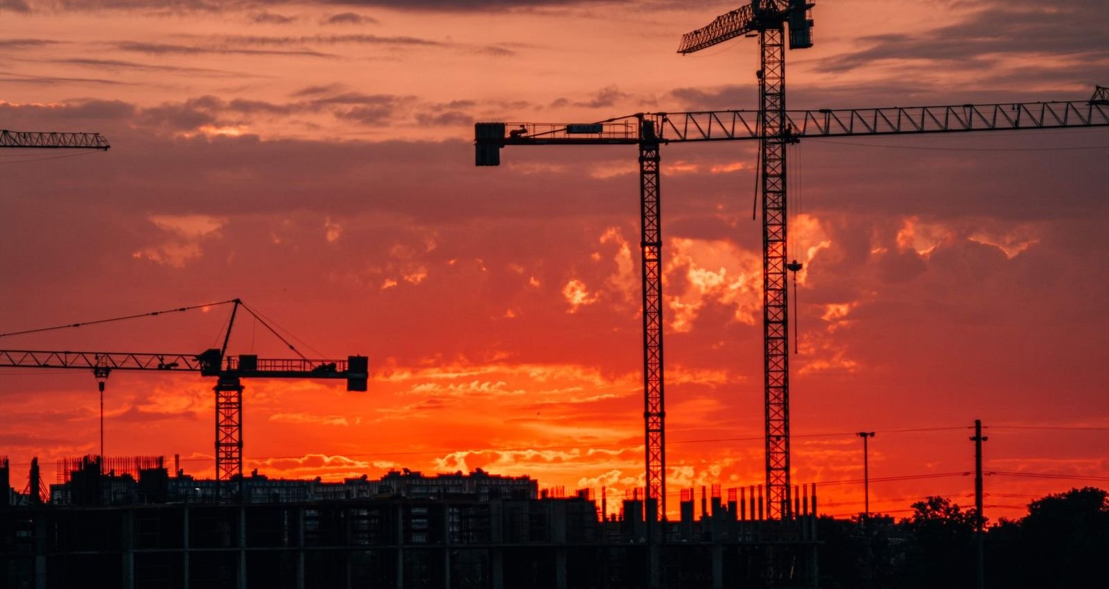 Construction cranes silhouetted against a red sunset sky