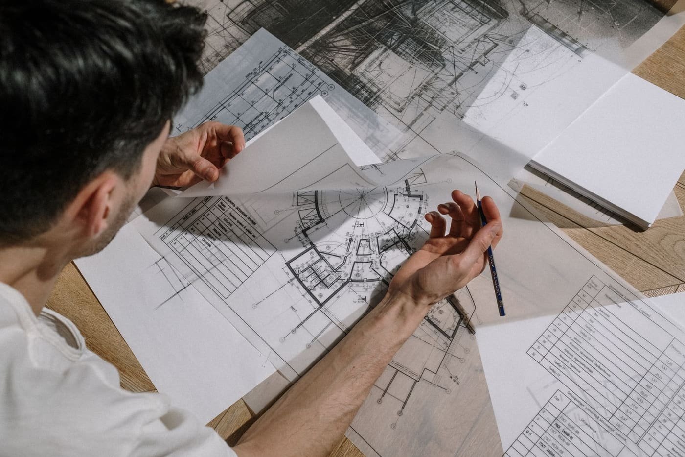 A designer studying and sketching over detailed architectural blueprints — reading a portfolio for structure, not just surface