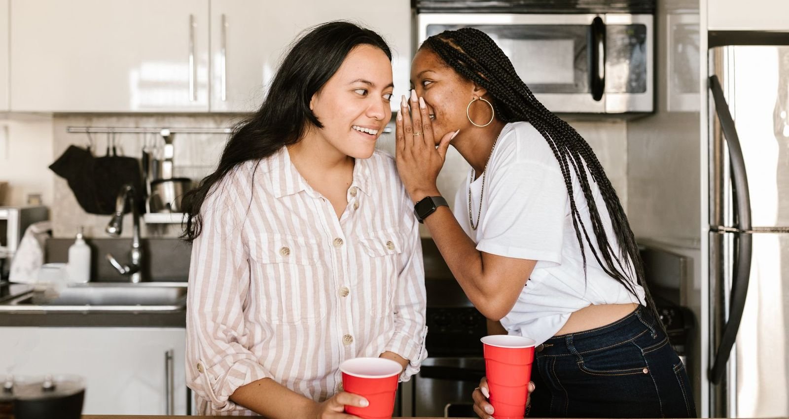 One woman whispering a recommendation to another in a kitchen