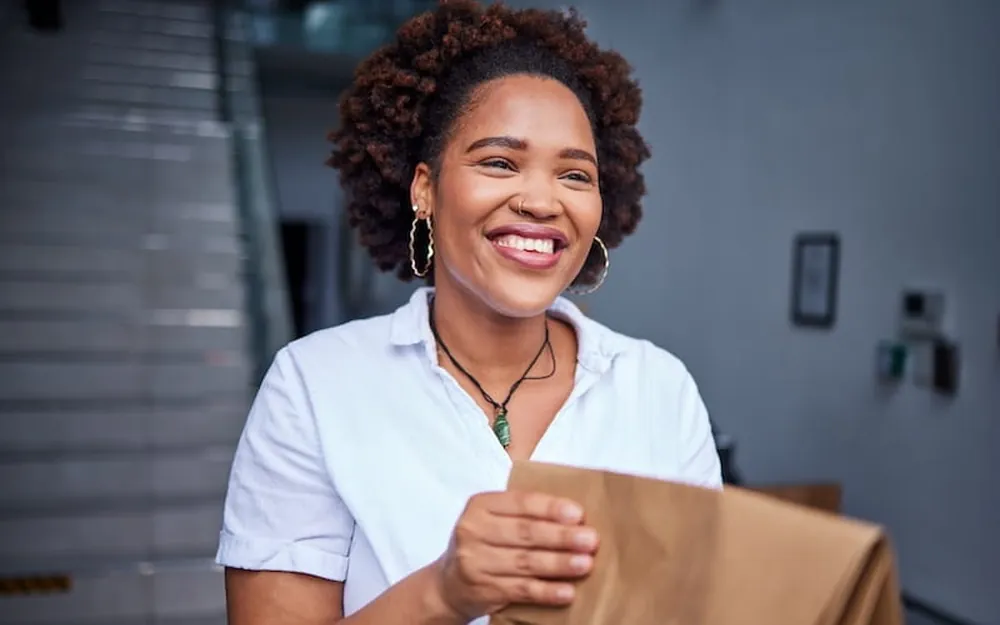 A smiling woman holding a wrapped parcel ready to ship