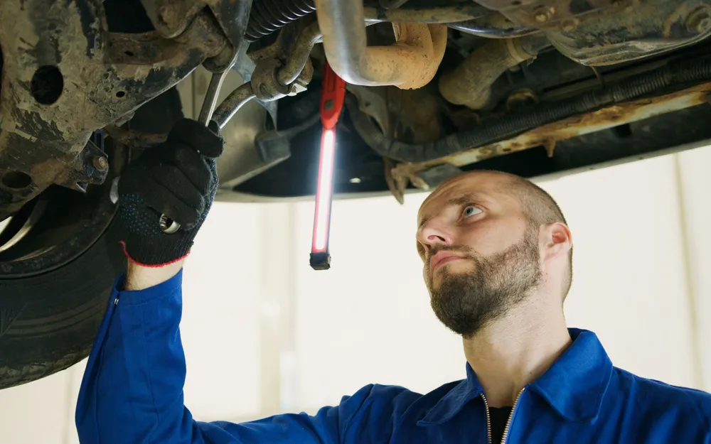 A mechanic under a car inspecting it with a flashlight