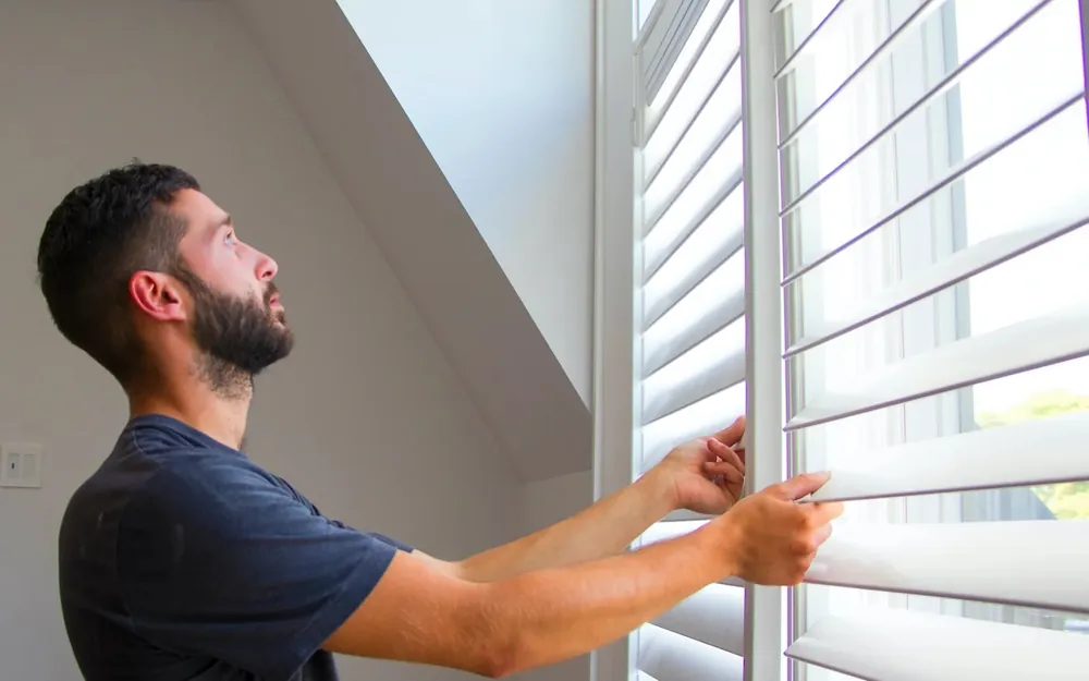 A tradesperson adjusting the slats of newly installed window shutters