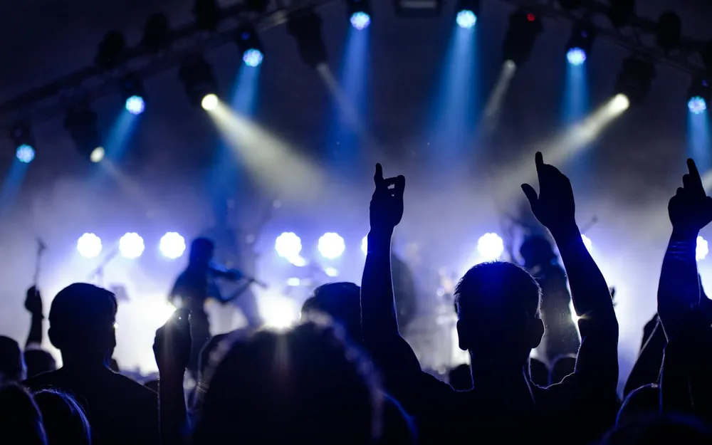 A crowd with raised hands silhouetted against stage lights at a concert