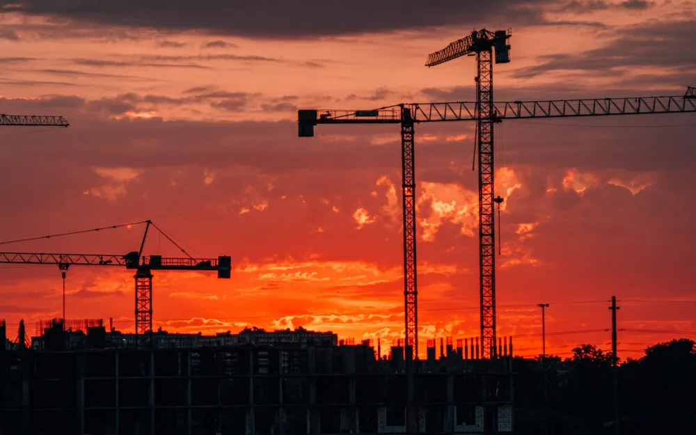 Construction cranes silhouetted against a red sunset sky