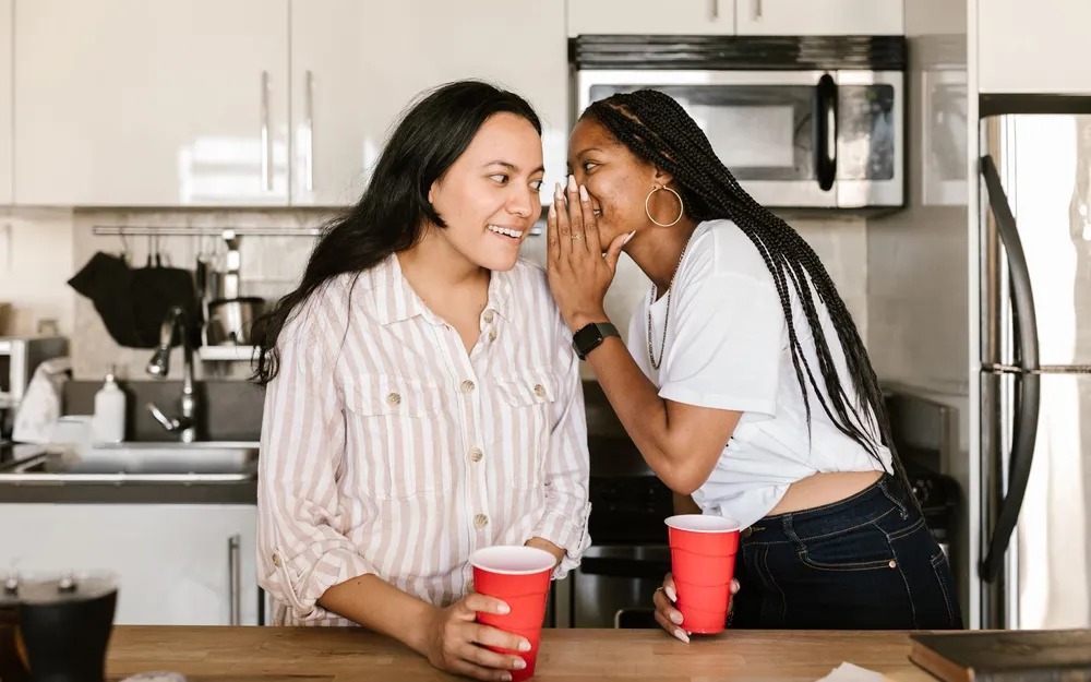 One woman whispering a recommendation to another in a kitchen
