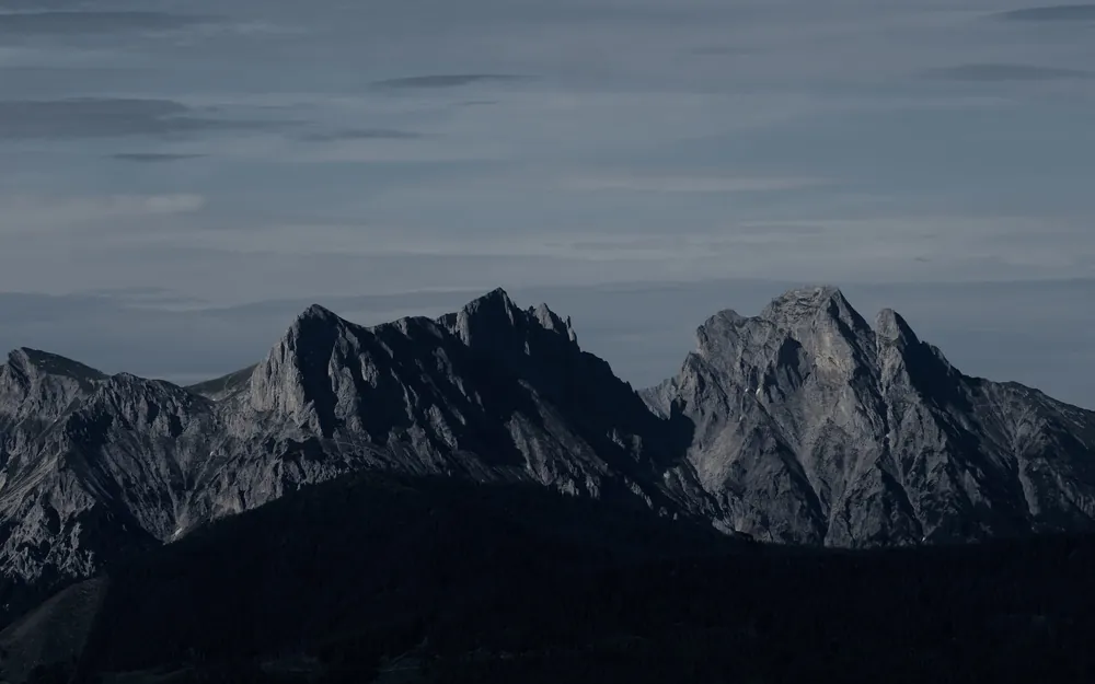 A dark mountain range with a sharp summit under overcast sky