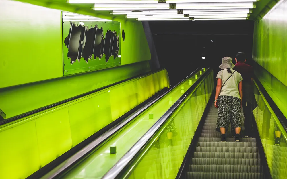 A person riding a green-lit escalator up out of a subway station