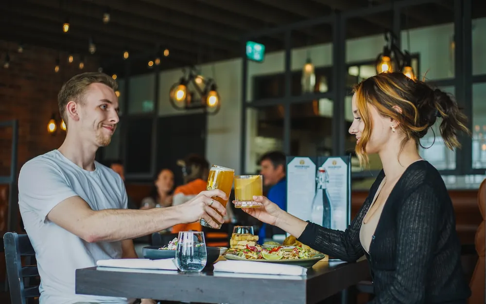 Two people raising drinks to each other across a restaurant table