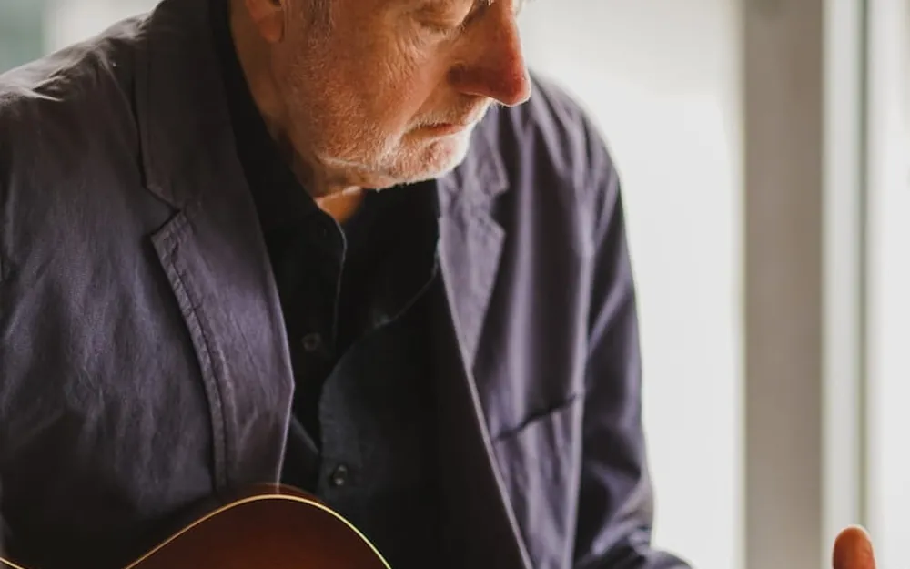 An older man playing an acoustic guitar in low window light