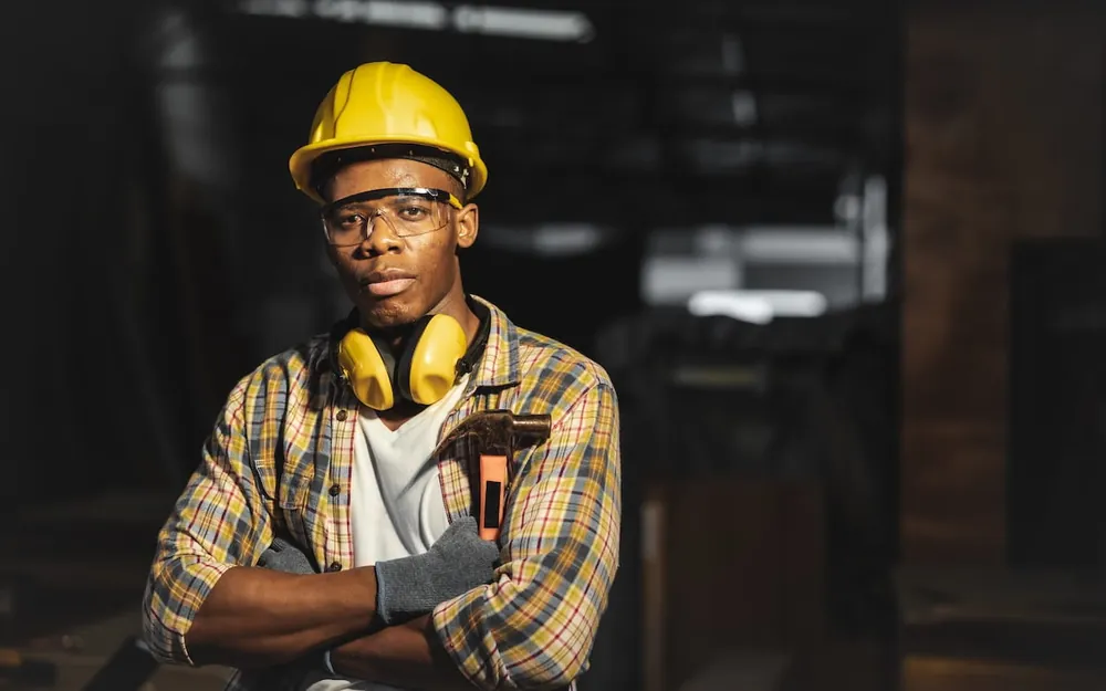 A construction worker in a hard hat and ear defenders standing with arms folded